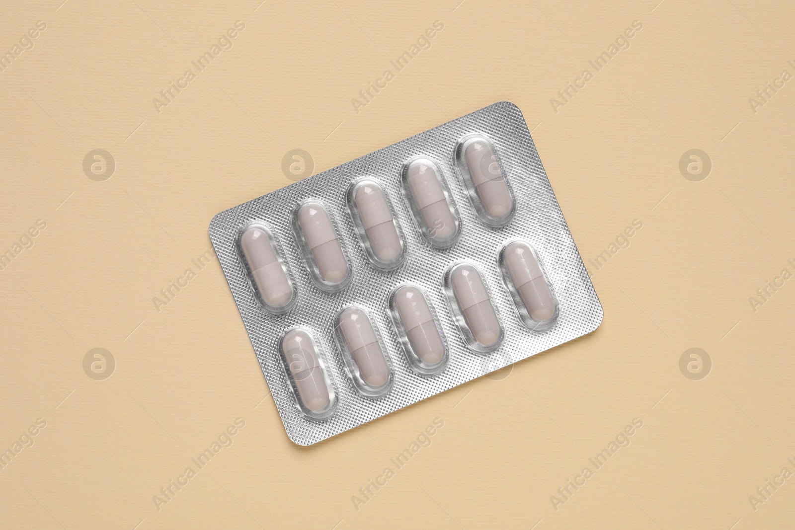 Photo of White pills in blister on beige background, top view