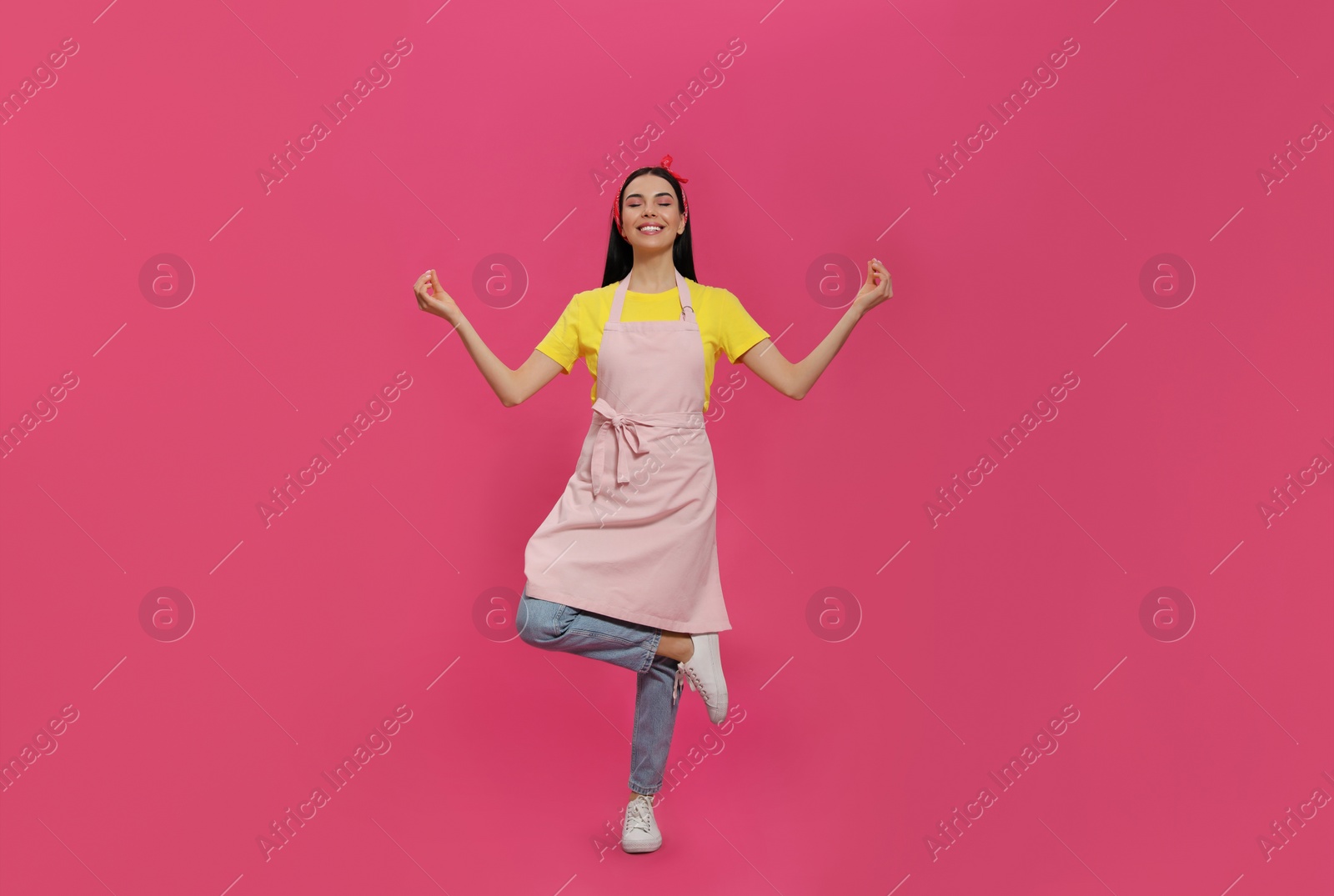 Photo of Young housewife wearing apron meditating on pink background