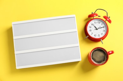 Blank letter board, alarm clock and coffee on yellow background, flat lay
