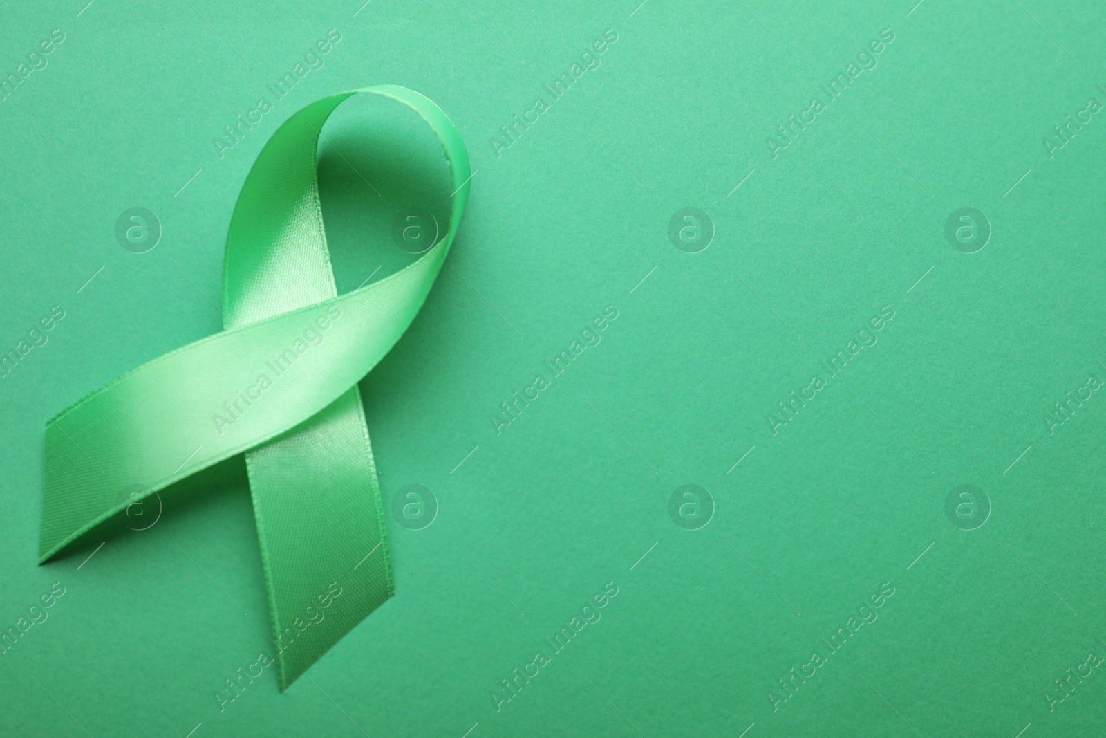 Photo of World Mental Health Day. Green ribbon on color background, top view with space for text