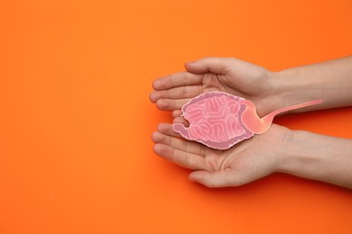 Photo of Woman holding paper cutout of small intestine on orange background, top view. Space for text