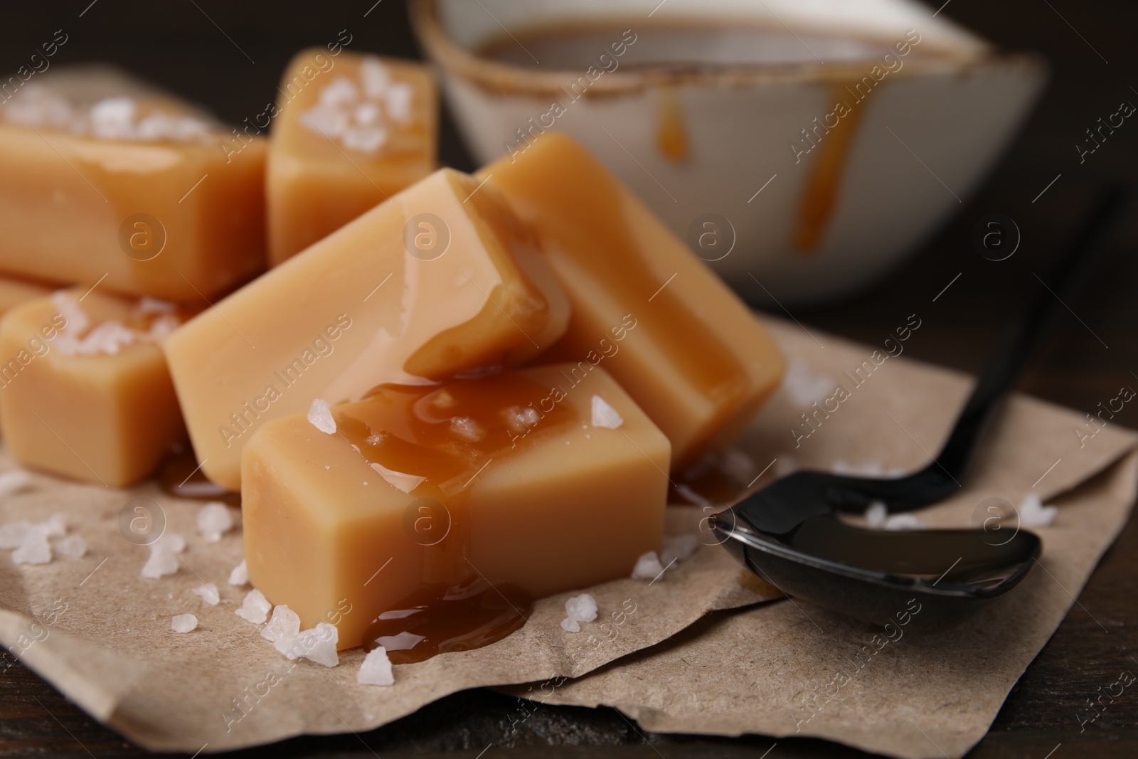 Photo of Delicious candies with sea salt and caramel sauce on wooden table, closeup