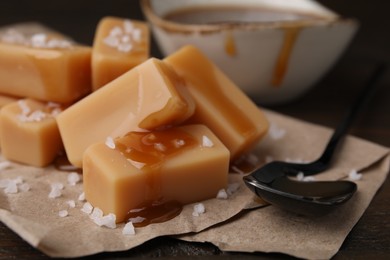 Photo of Delicious candies with sea salt and caramel sauce on wooden table, closeup