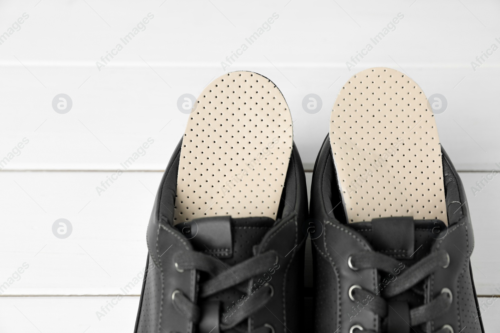 Photo of Orthopedic insoles in shoes on white wooden floor, closeup. Space for text