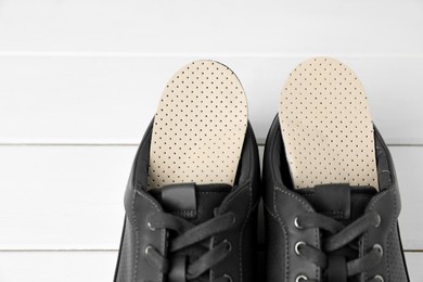 Photo of Orthopedic insoles in shoes on white wooden floor, closeup. Space for text