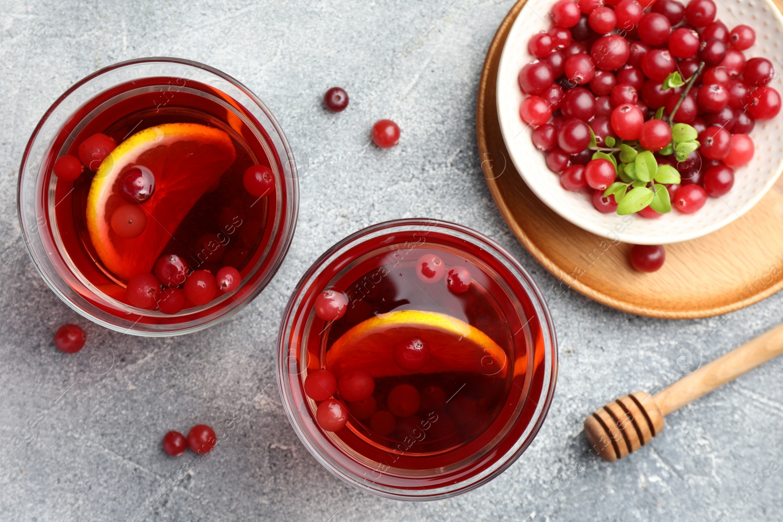 Photo of Tasty hot cranberry tea with lemon in glasses and fresh berries on light grey textured table