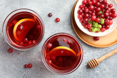 Tasty hot cranberry tea with lemon in glasses and fresh berries on light grey textured table