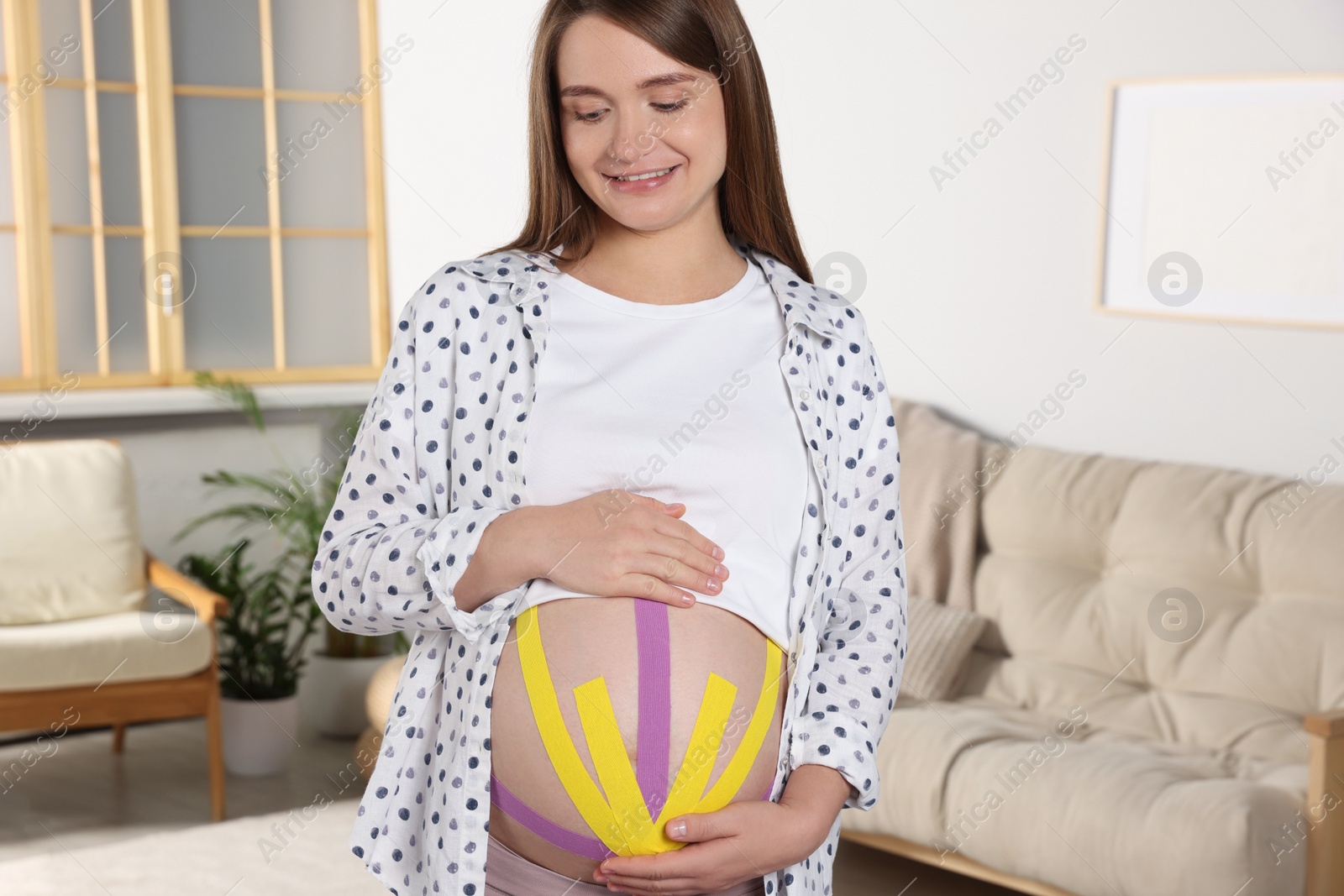 Photo of Pregnant woman with kinesio tapes on her belly at home