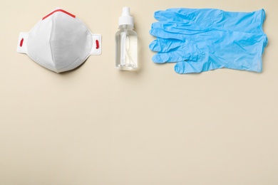 Photo of Medical gloves, respiratory mask and hand sanitizer on beige background, flat lay. Space for text
