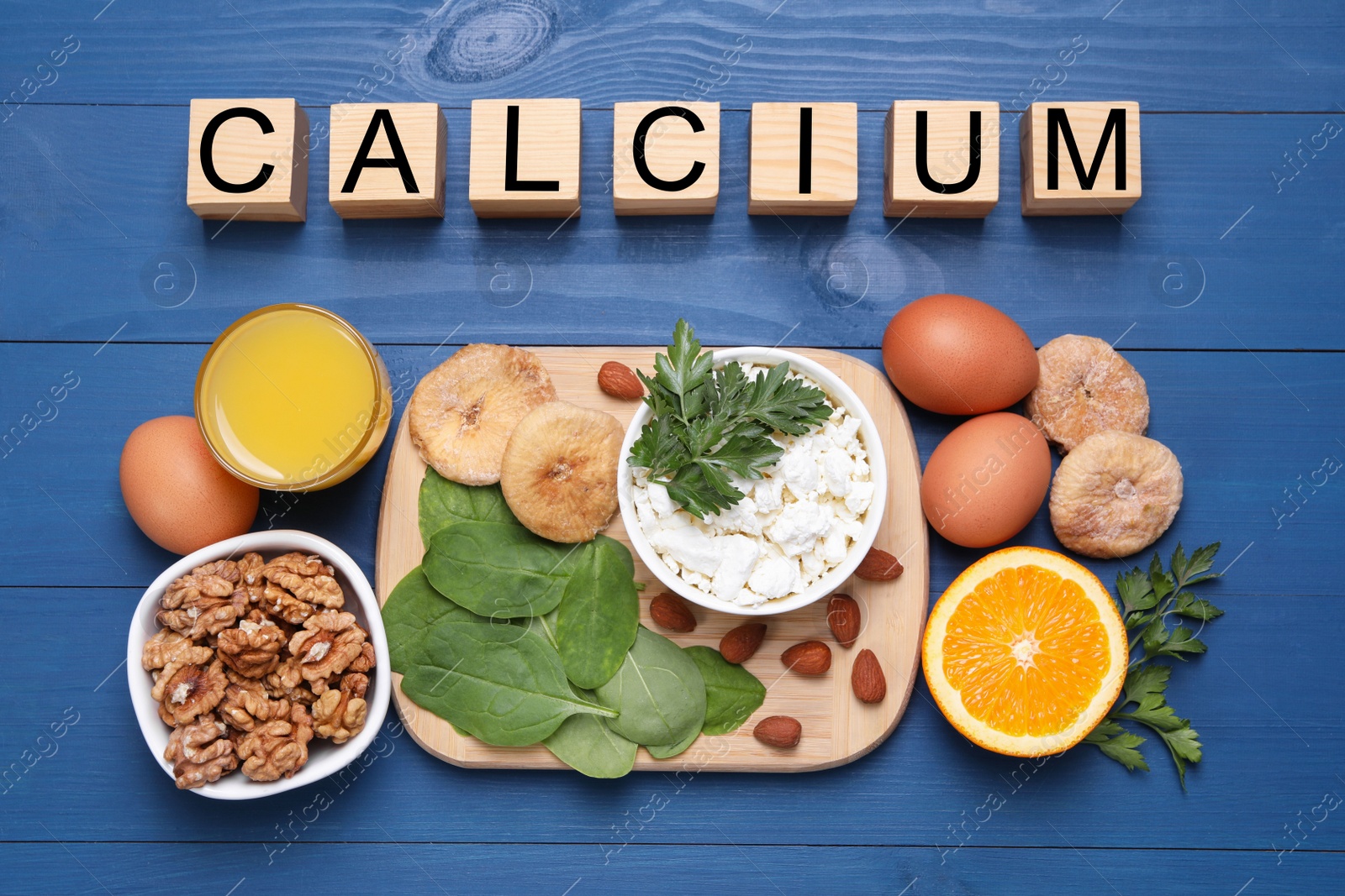 Photo of Word Calcium made of wooden cubes and natural food on blue table, flat lay