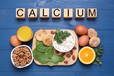 Word Calcium made of wooden cubes and natural food on blue table, flat lay