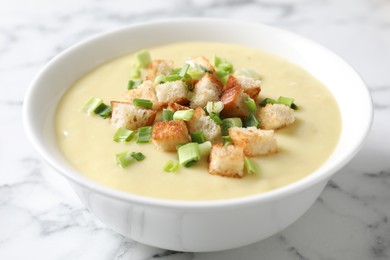 Photo of Tasty potato soup with croutons and green onion in bowl on white marble table, closeup