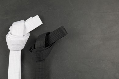 Photo of White and black karate belts on gray background, flat lay. Space for text