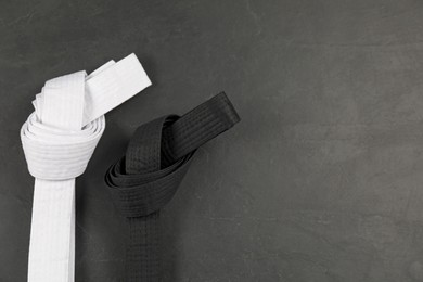 White and black karate belts on gray background, flat lay. Space for text