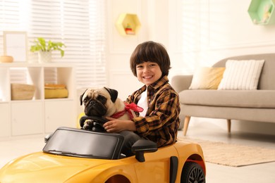 Photo of Little boy with his dog in toy car at home