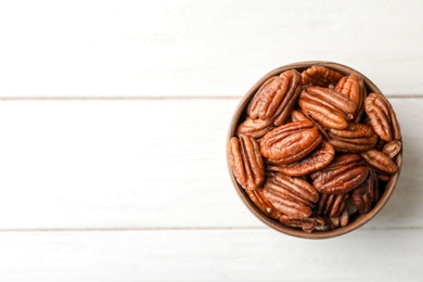 Shelled pecan nuts in bowl and space for text on wooden background, top view