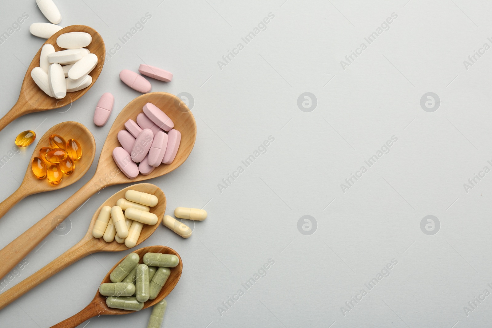 Photo of Different vitamin pills in spoons on light grey background, flat lay and space for text. Health supplement