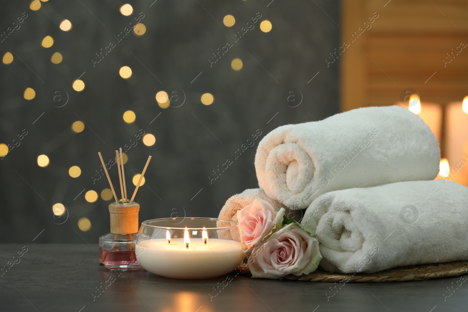 Photo of Spa composition with burning candle and towels on grey table