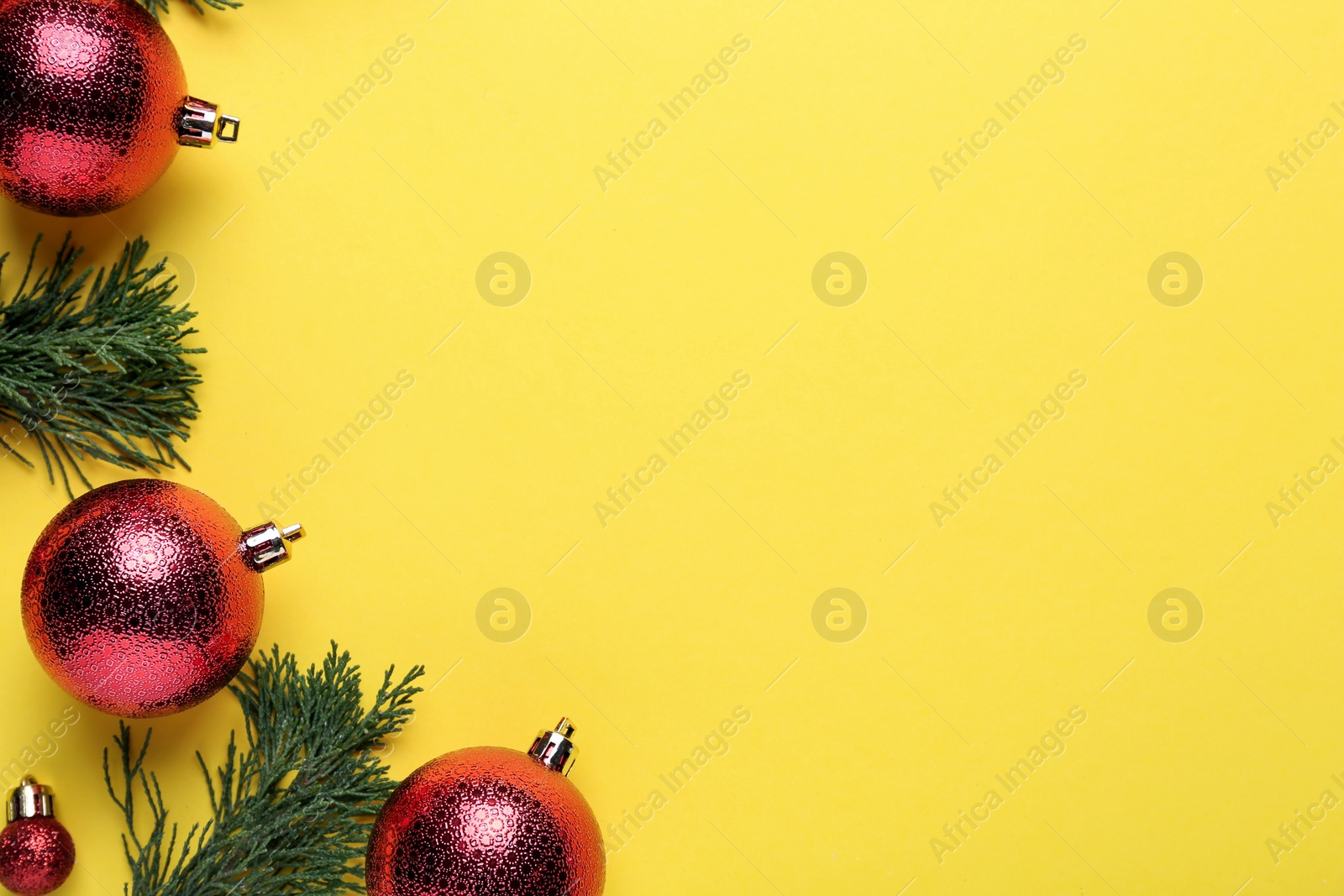 Photo of Beautiful red Christmas balls and fir branches on yellow background, flat lay. Space for text