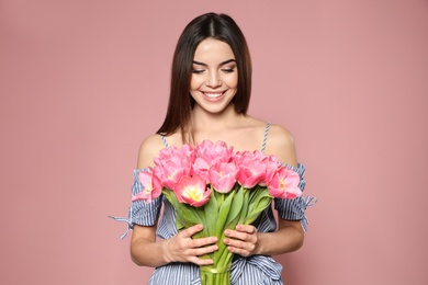 Photo of Portrait of beautiful smiling girl with spring tulips on pink background. International Women's Day