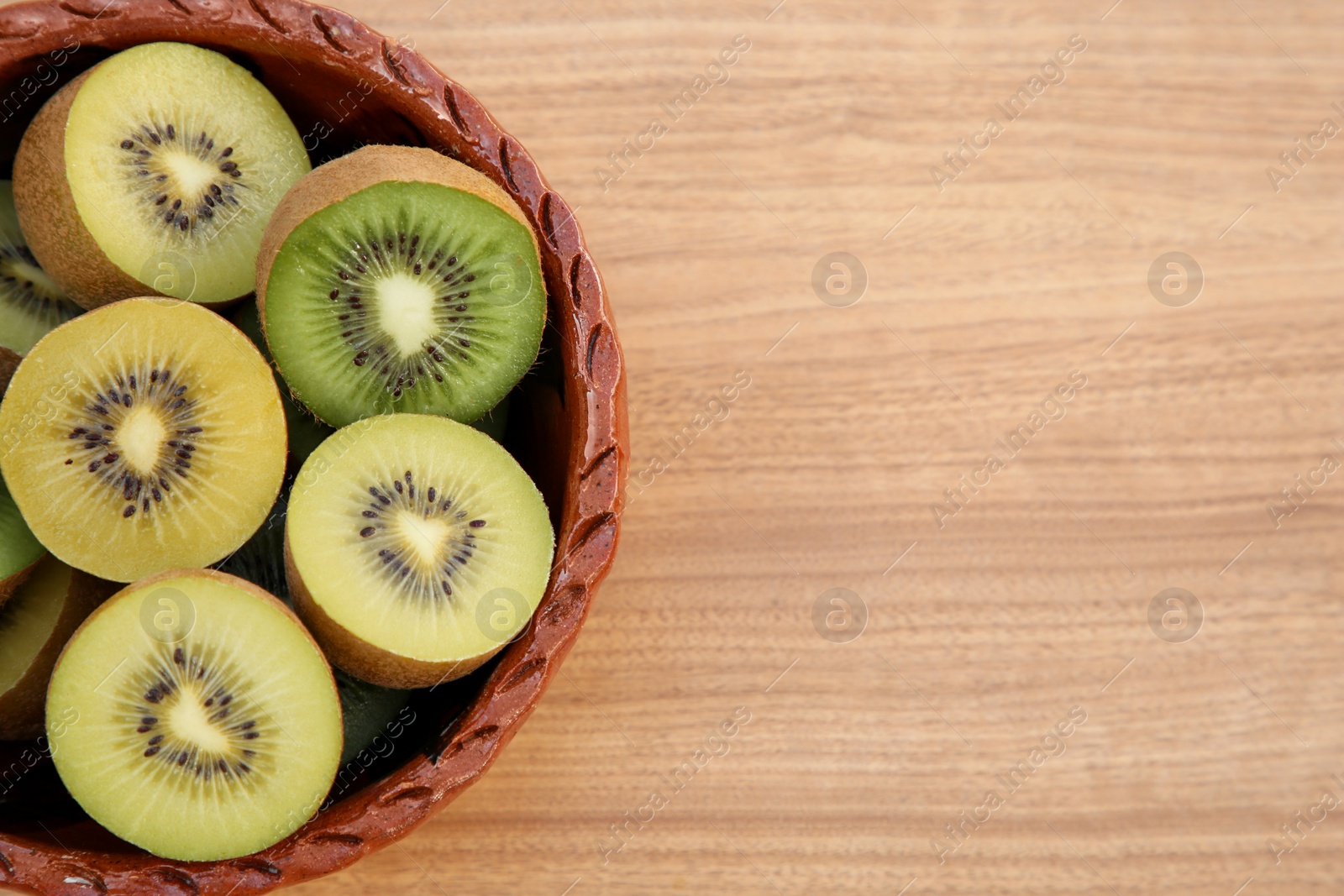 Photo of Bowl of many cut fresh kiwis on wooden table, top view. Space for text