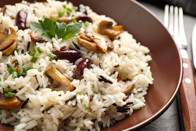 Delicious rice pilaf with mushrooms and beans in plate, closeup