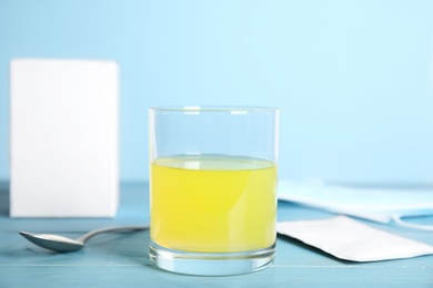 Glass of dissolved medicine, spoon with powder and sachet on blue wooden table