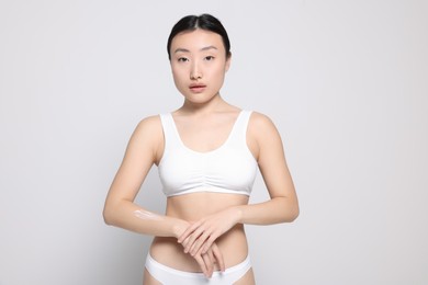 Photo of Beautiful young Asian woman with body cream smear on arm against light grey background