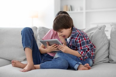 Photo of Happy brother and sister with tablet on sofa at home