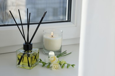 Aromatic reed air freshener, freesia flowers and burning candle on windowsill