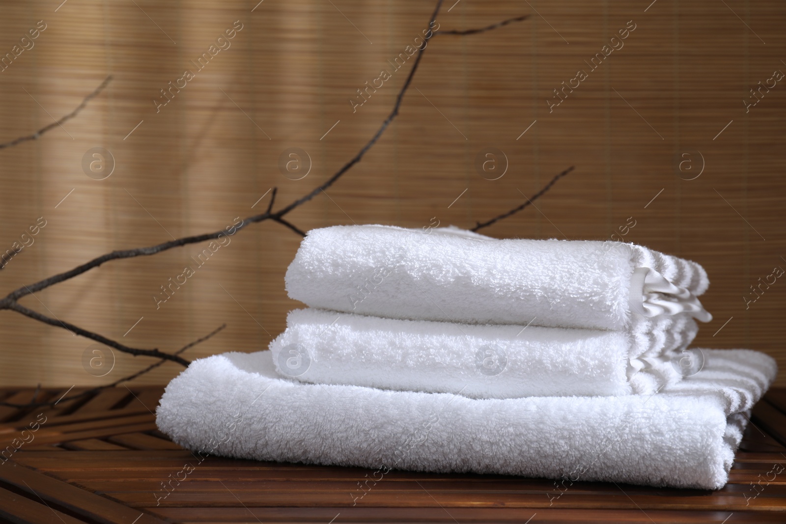 Photo of Stacked soft towels on wooden table and tree branches indoors