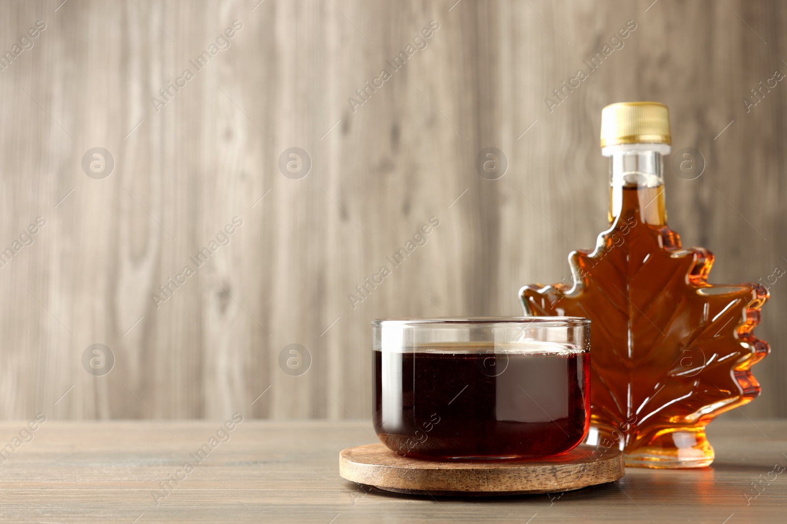 Photo of Bottle and bowl of tasty maple syrup on wooden table, space for text