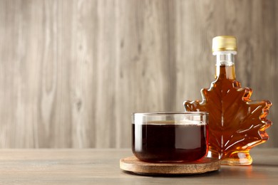 Bottle and bowl of tasty maple syrup on wooden table, space for text