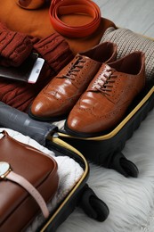 Photo of Open suitcase with folded clothes, accessories and shoes on floor, closeup