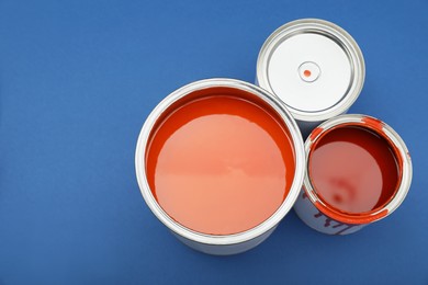 Photo of Cans of orange paint on blue background, flat lay. Space for text