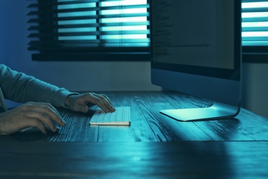 Photo of Man using computer in dark room, closeup. Criminal offence
