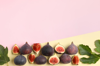 Delicious ripe figs and green leaves on color background, flat lay. Space for text