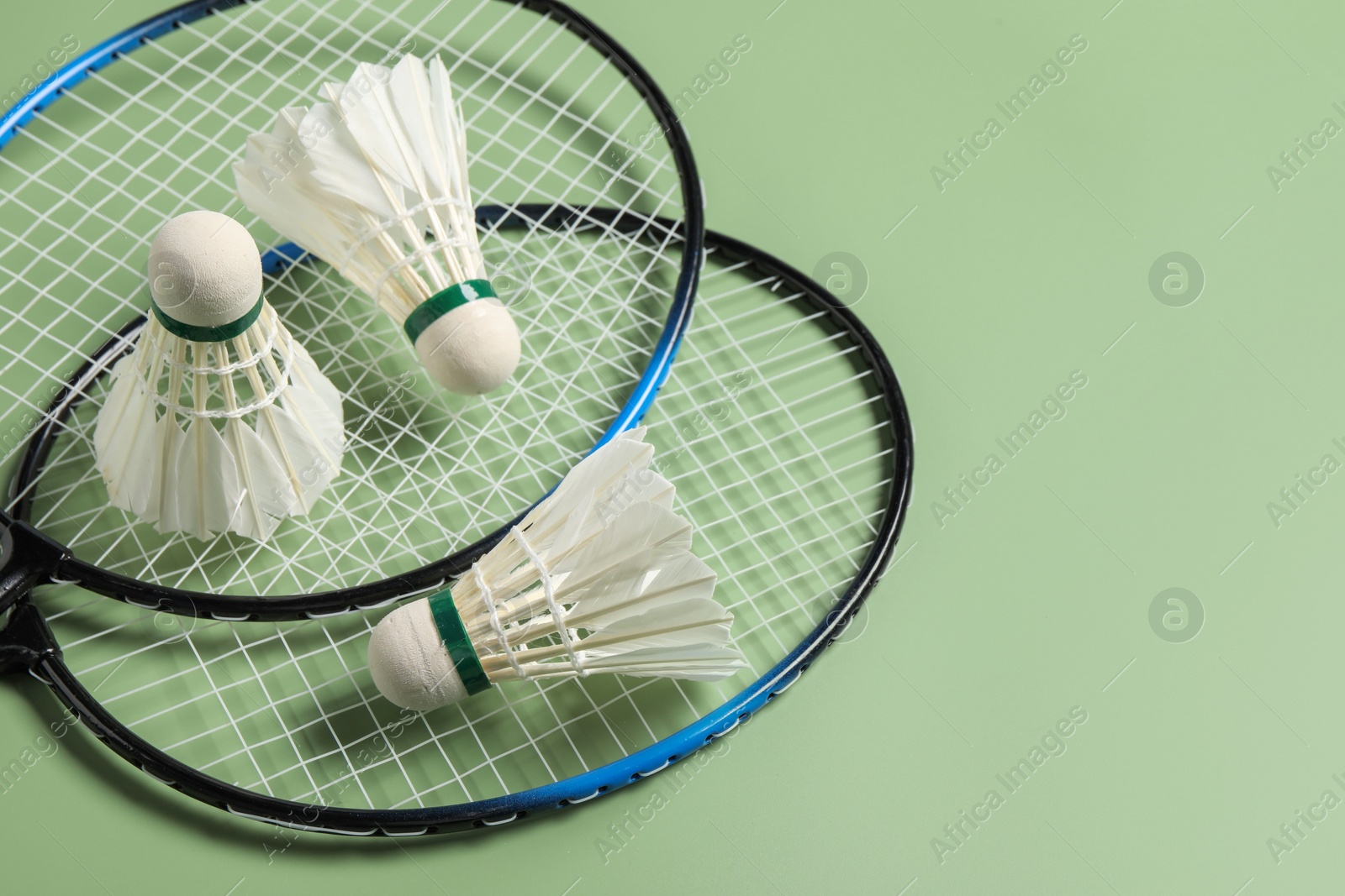 Photo of Feather badminton shuttlecocks and rackets on green background, above view. Space for text