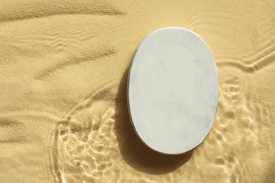 Photo of Stylish presentation for product. Stone podium in water on sand, top view. Space for text