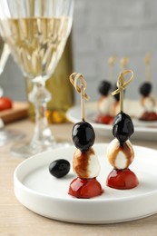 Photo of Tasty canapes with black olives, mozzarella and cherry tomatoes on light wooden table, closeup