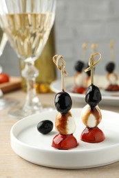 Tasty canapes with black olives, mozzarella and cherry tomatoes on light wooden table, closeup