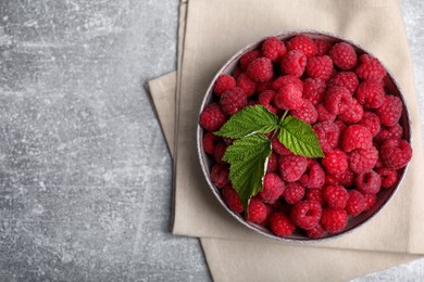 Photo of Bowl of fresh ripe raspberries with green leaves on grey table, top view. Space for text