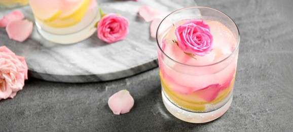 Delicious refreshing drink with lemon and roses on grey table. Banner design