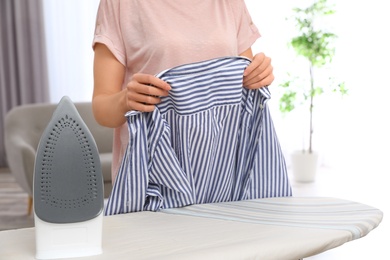 Young woman ironing clothes on board at home, closeup