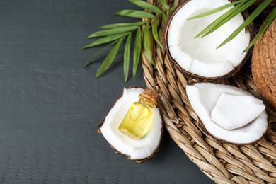 Bottle of organic coconut cooking oil, leaves and fresh fruits on grey wooden table, above view. Space for text