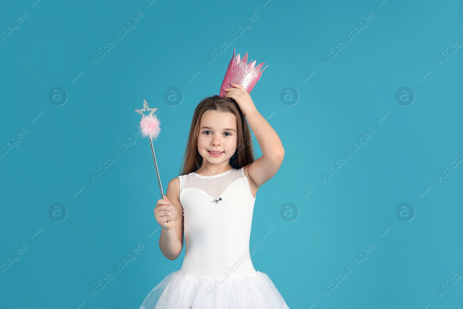 Photo of Cute girl in pink crown with magic wand on light blue background. Little princess