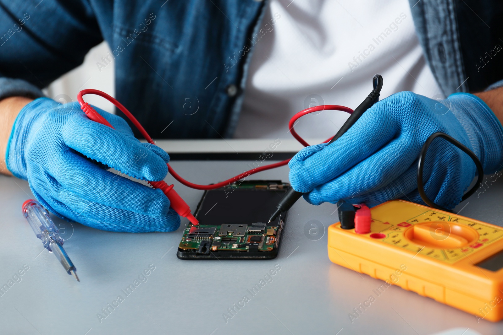 Photo of Technician checking broken smartphone at table in repair shop, closeup