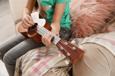 Photo of Little girl playing guitar on sofa in room