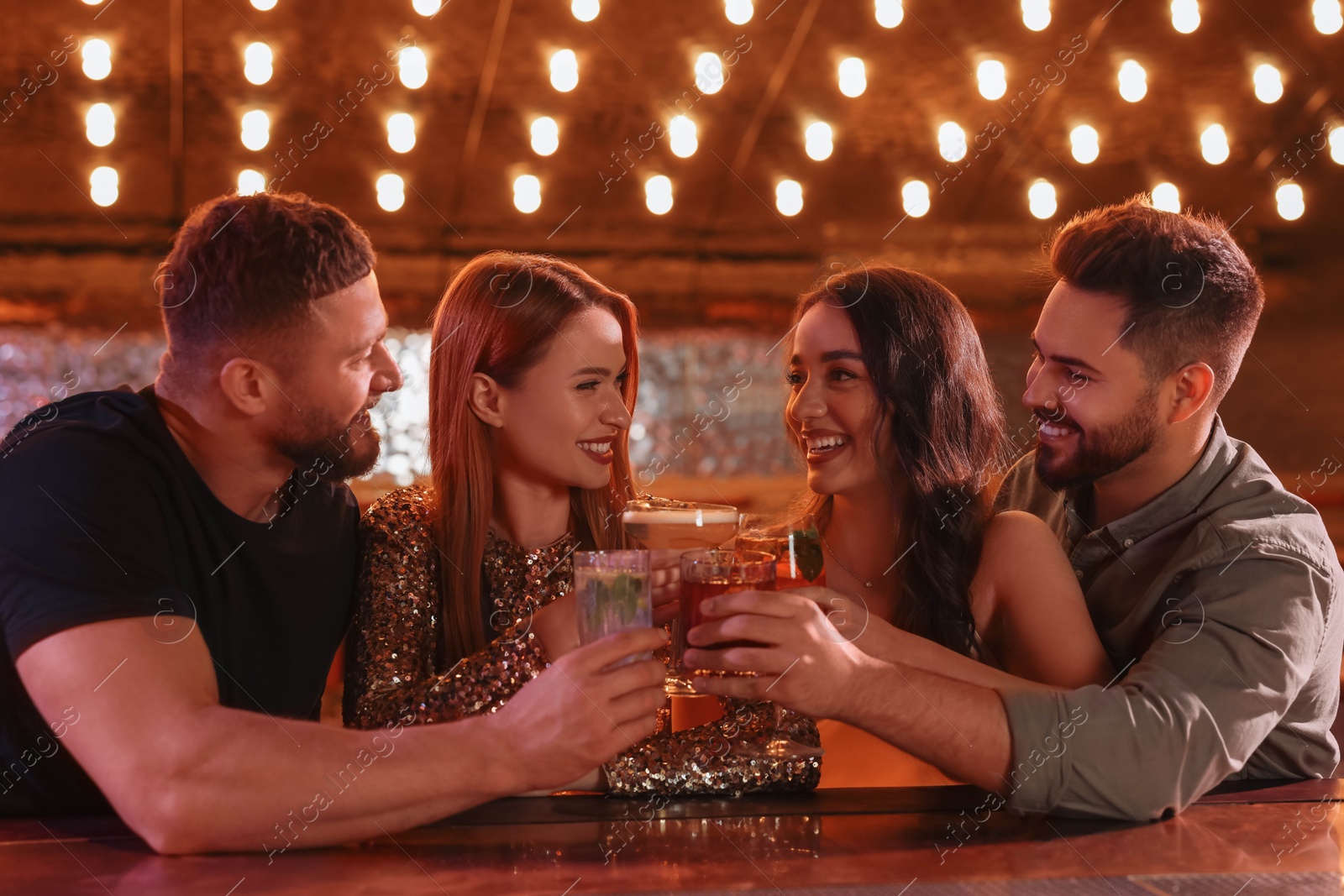 Photo of Happy friends clinking glasses with fresh cocktails in bar