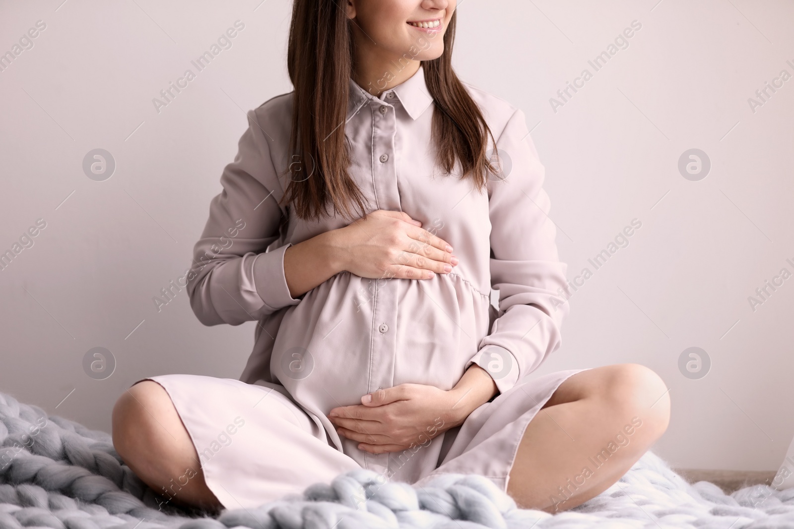 Photo of Young pregnant woman sitting on warm blanket indoors